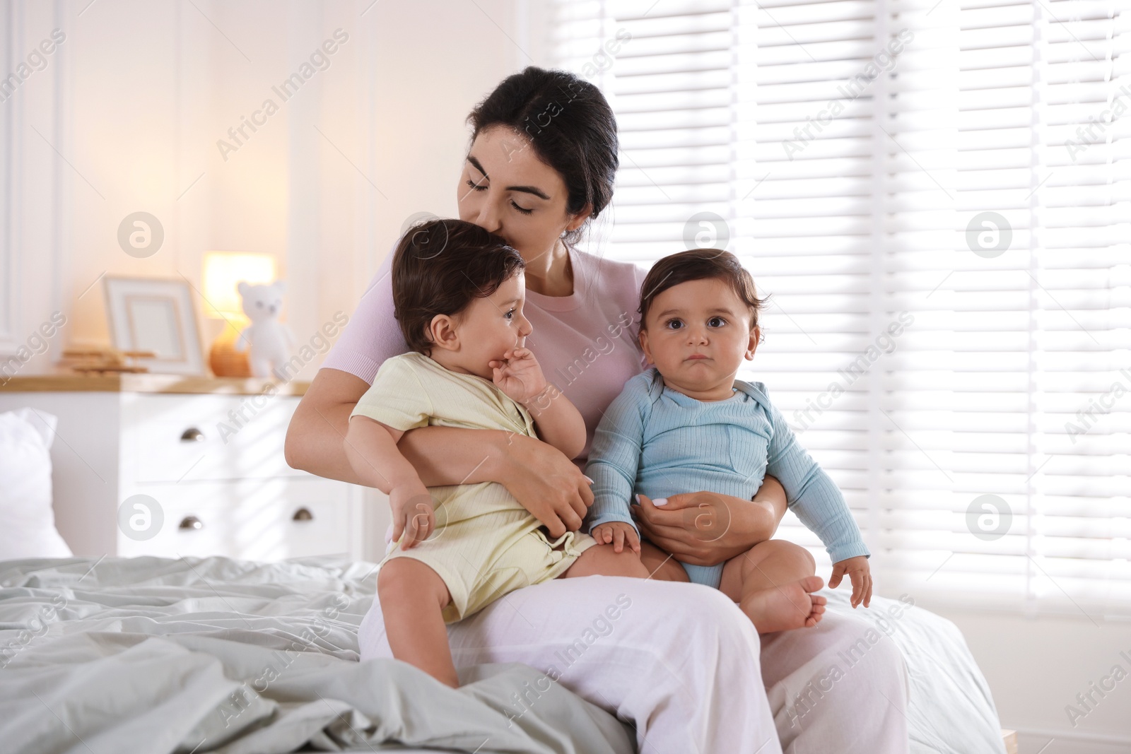 Photo of Mother with her cute little twin babies on bed indoors