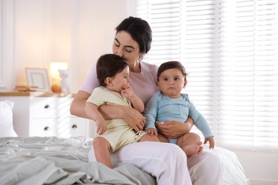 Photo of Mother with her cute little twin babies on bed indoors