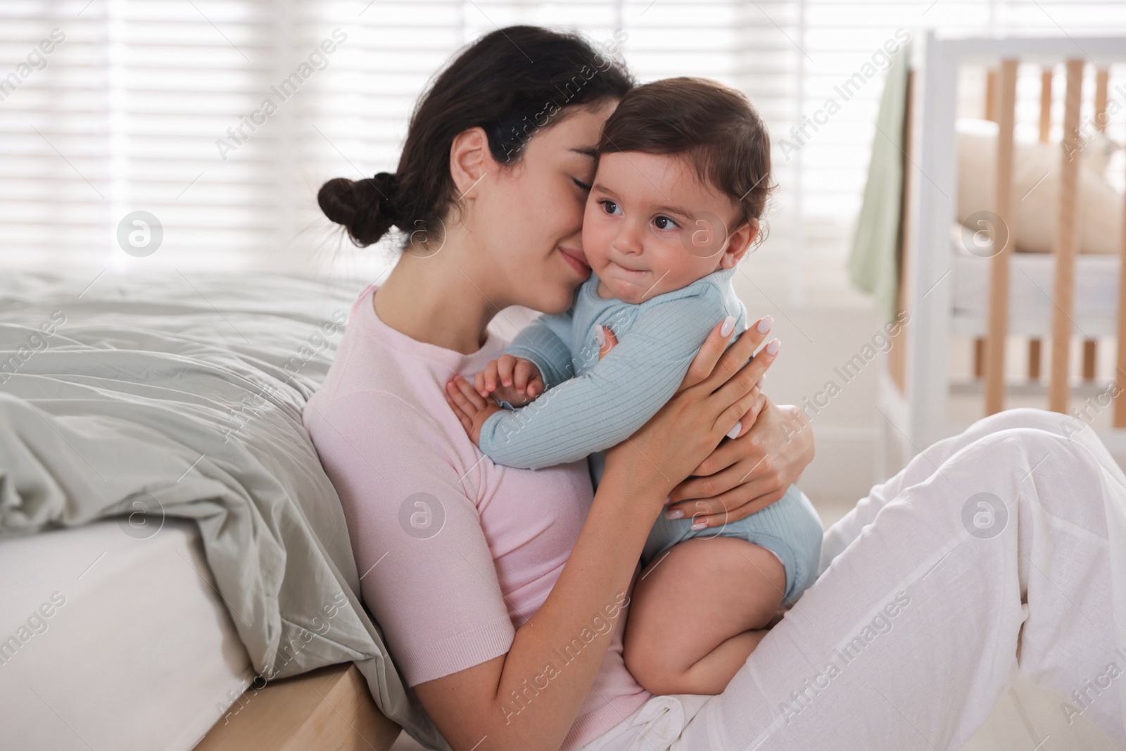 Photo of Mother with her cute little baby near bed indoors