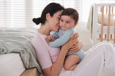 Photo of Mother with her cute little baby near bed indoors