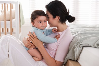 Photo of Mother with her cute little baby near bed indoors