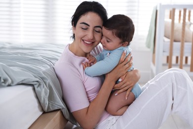 Photo of Mother with her cute little baby near bed indoors