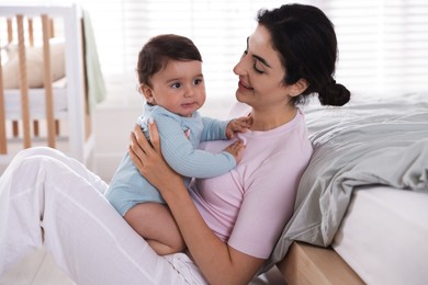 Photo of Mother with her cute little baby near bed indoors