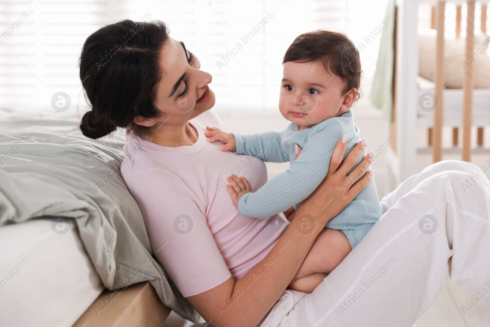 Photo of Mother with her cute little baby near bed indoors