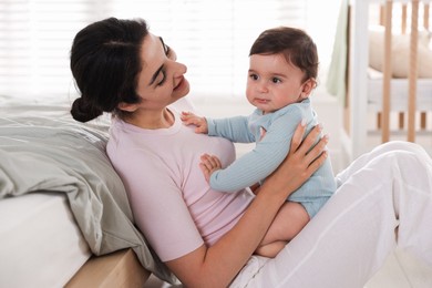 Photo of Mother with her cute little baby near bed indoors