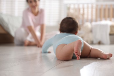Photo of Mother with her cute little baby on floor indoors, selective focus