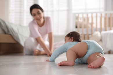 Photo of Mother with her cute little baby on floor indoors, selective focus