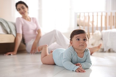 Photo of Mother with her cute little baby on floor indoors, selective focus