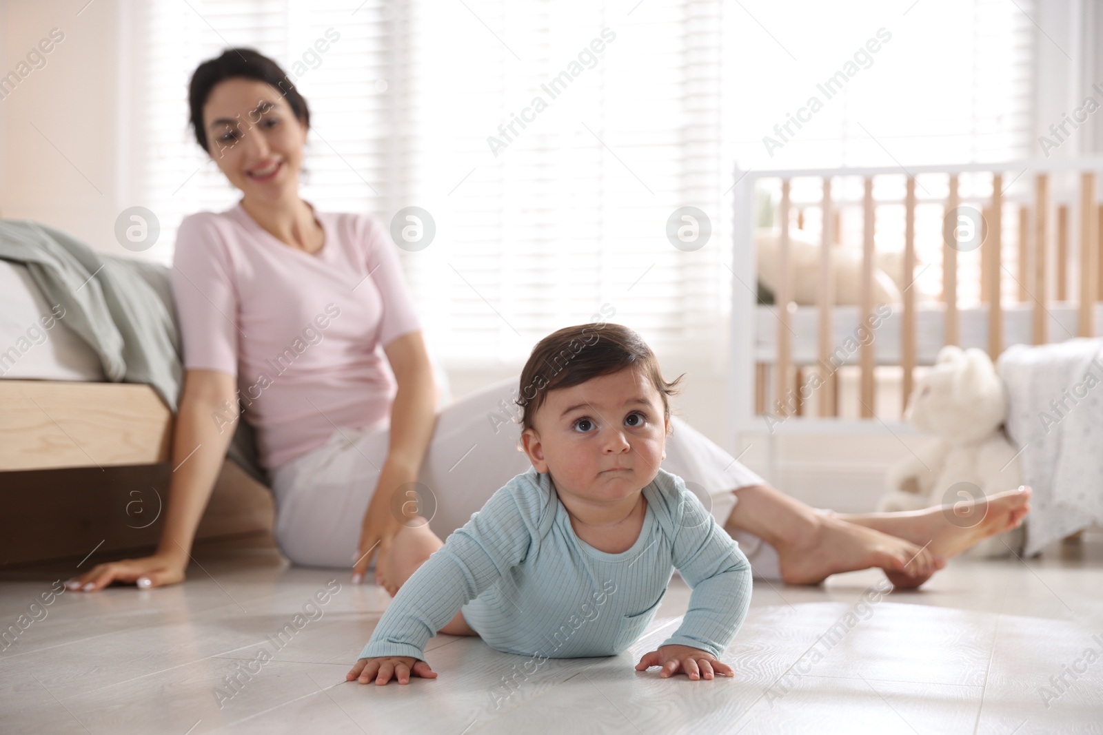 Photo of Mother with her cute little baby on floor indoors, selective focus