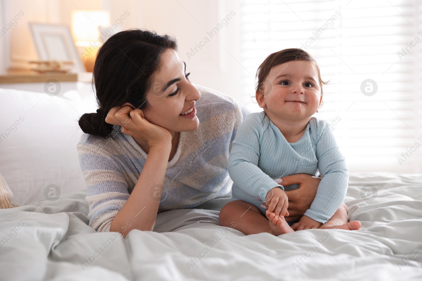 Photo of Mother with her cute little baby on bed indoors