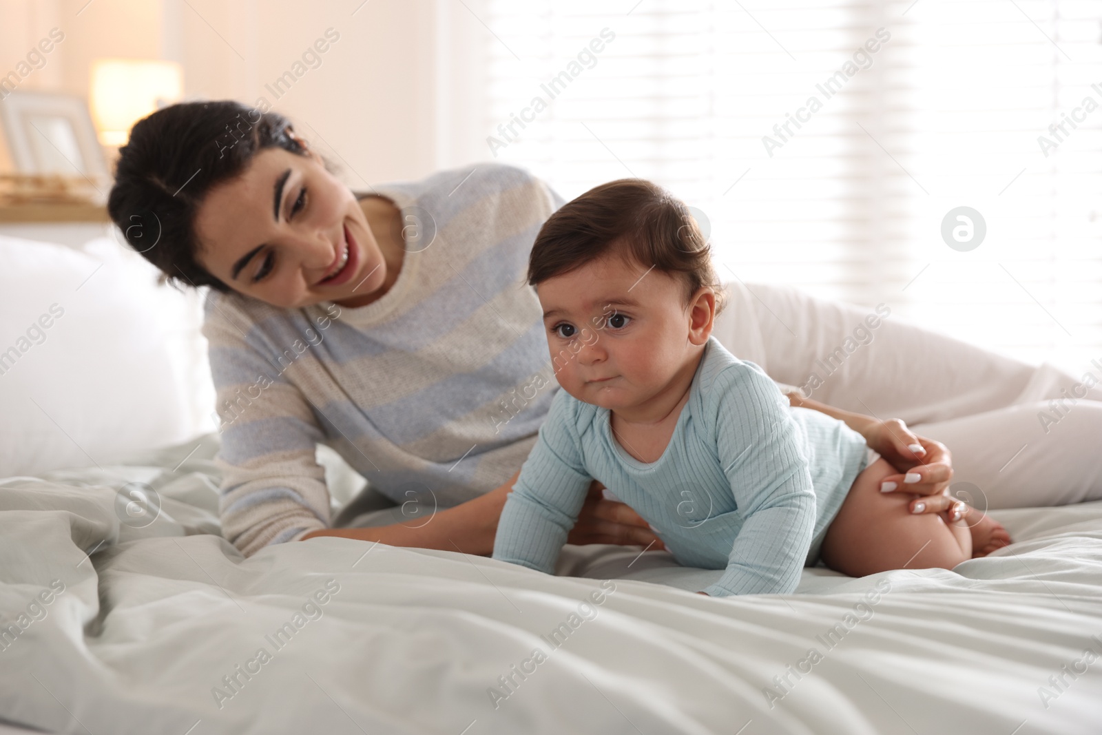 Photo of Mother with her cute little baby on bed indoors