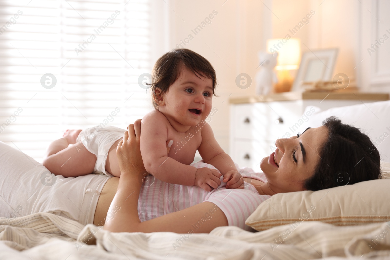 Photo of Mother with her cute little baby on bed indoors
