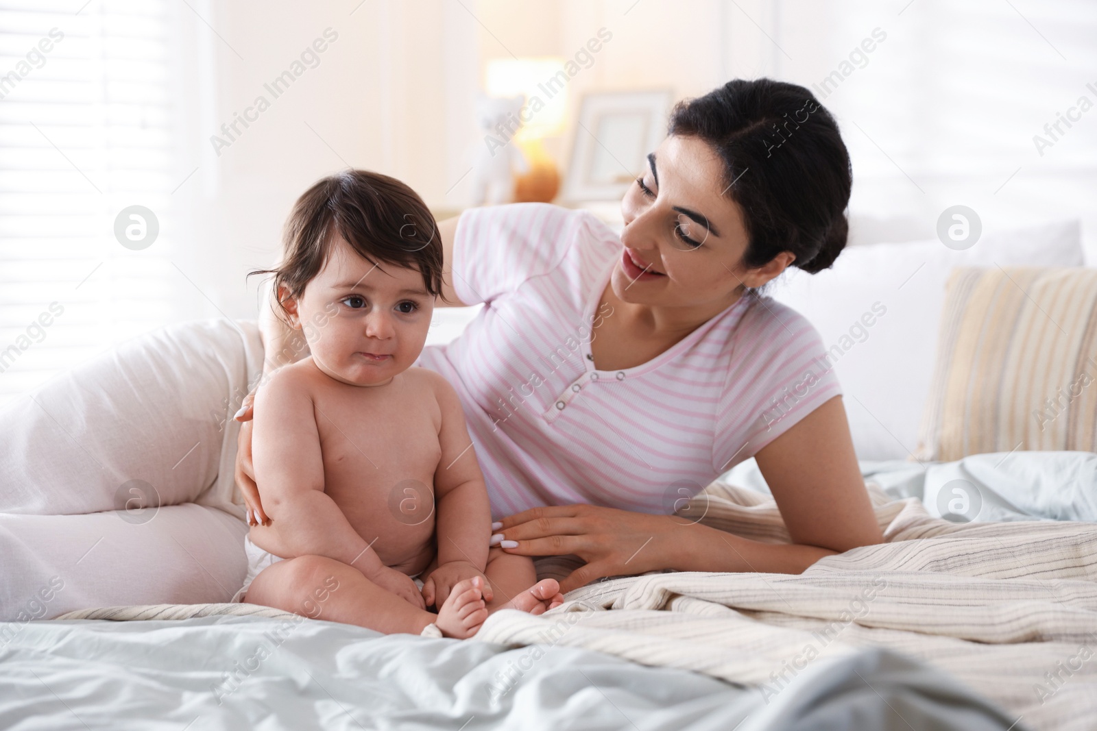 Mother with her cute little baby on bed indoors Photo of Mother with her cute little baby on bed indoors