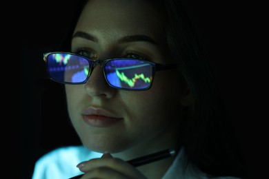 Photo of Young woman wearing glasses with reflection on dark background, closeup