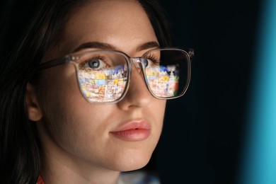 Photo of Young woman wearing glasses with reflection on dark background, closeup