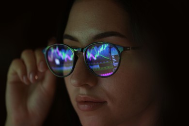 Photo of Young woman wearing glasses with reflection on dark background, closeup