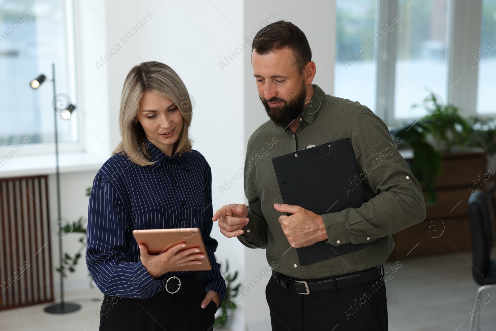 Smiling business partners with tablet and clipboard working together in office Photo of Smiling business partners with tablet and clipboard working together in office