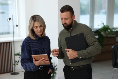 Photo of Smiling business partners with tablet and clipboard working together in office