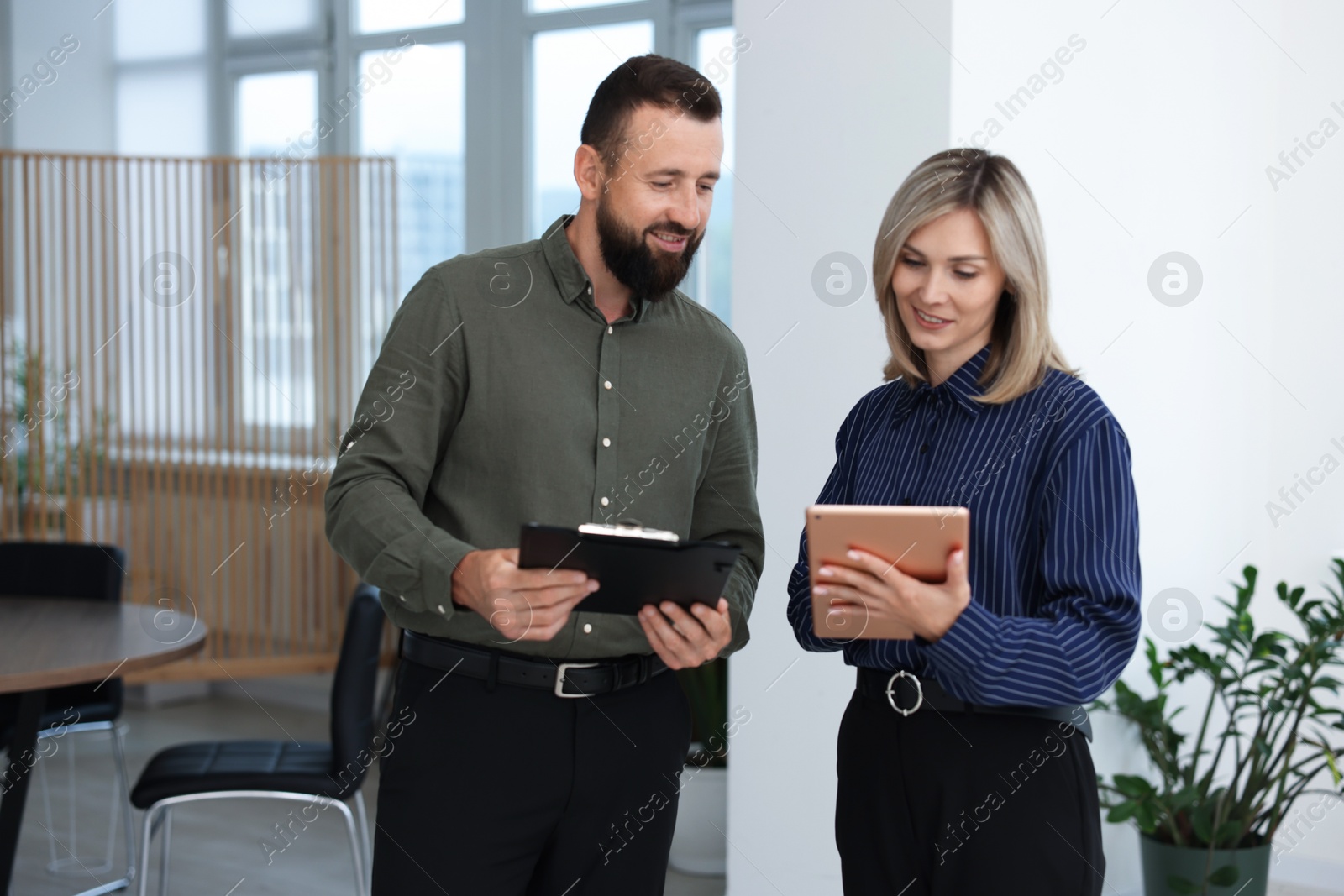 Smiling business partners with tablet and clipboard working together in office Photo of Smiling business partners with tablet and clipboard working together in office
