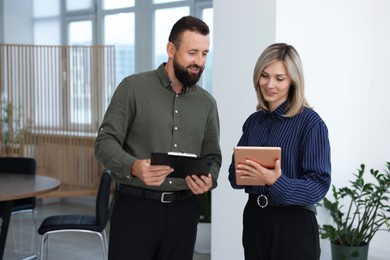 Photo of Smiling business partners with tablet and clipboard working together in office