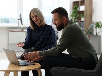Photo of Smiling business partners working with laptop at table in office