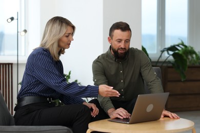 Photo of Smiling business partners working with laptop at table in office