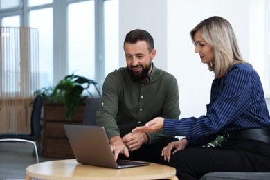 Photo of Smiling business partners working with laptop at table in office