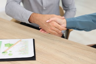 Photo of Business partners shaking hands at wooden table indoors, closeup