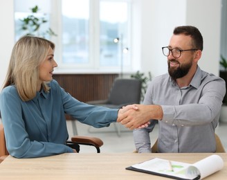 Photo of Smiling business partners shaking hands at table in office