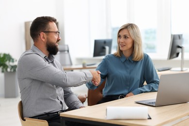 Photo of Smiling business partners shaking hands at table in office