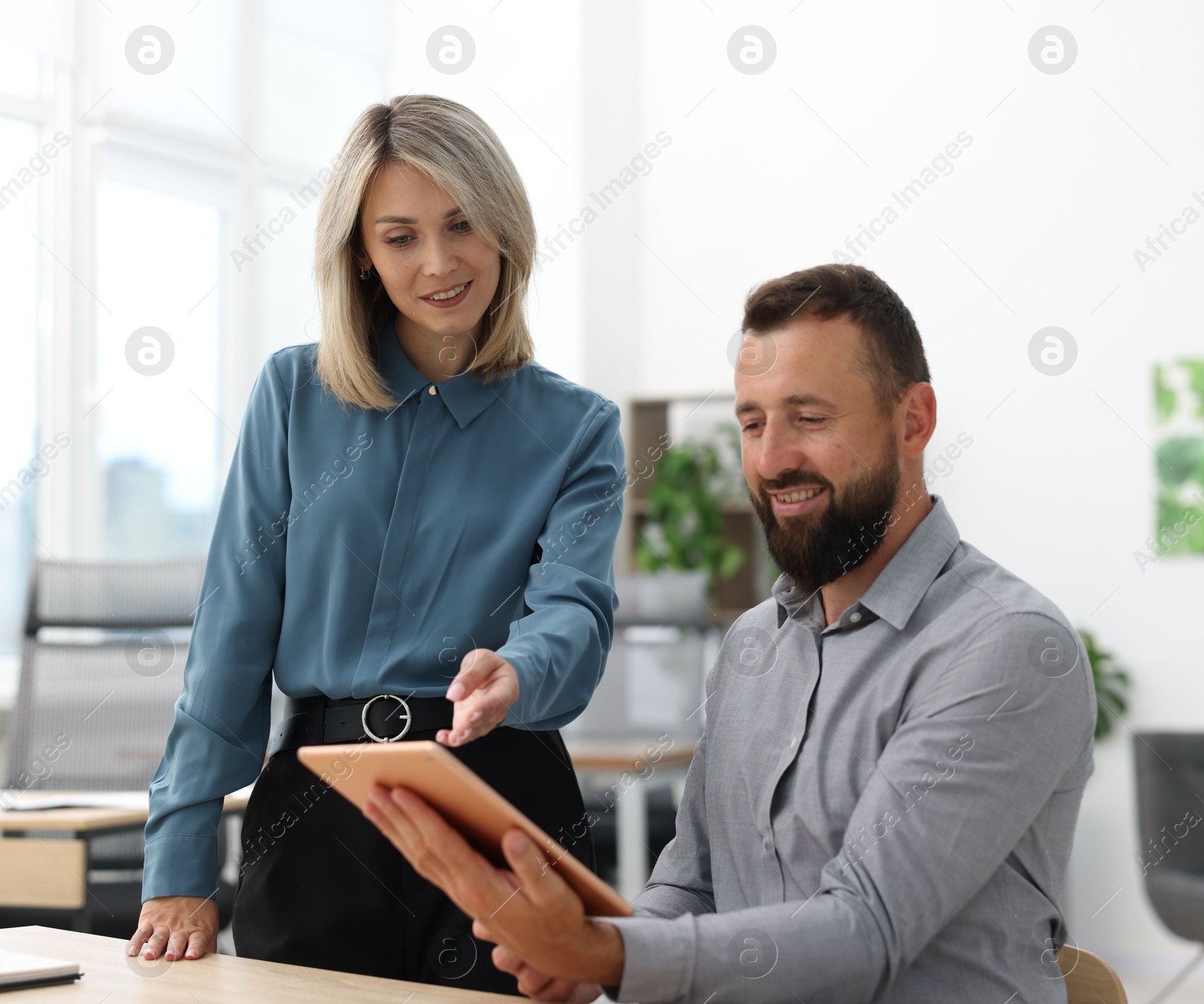 Photo of Smiling business partners working with tablet at table in office