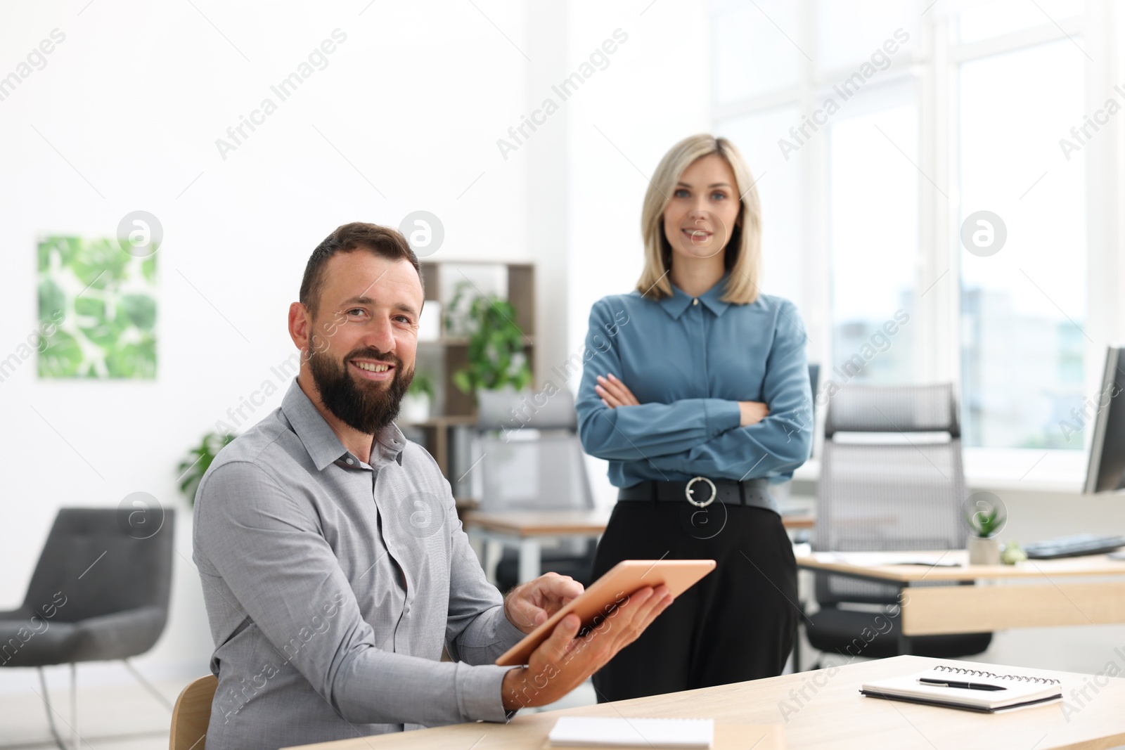 Portrait of smiling business partners with tablet at table in office Photo of Portrait of smiling business partners with tablet at table in office