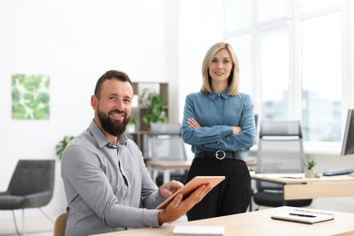 Photo of Portrait of smiling business partners with tablet at table in office