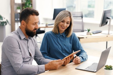Photo of Smiling business partners working with tablet at table in office