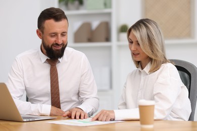 Photo of Smiling business partners working with documents at table in office
