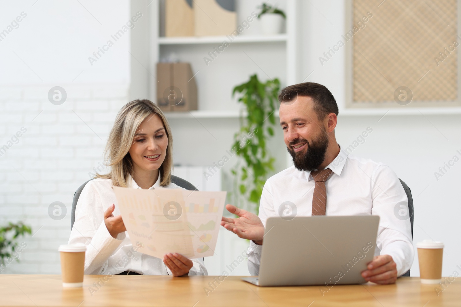 Smiling business partners working with documents at table in office Photo of Smiling business partners working with documents at table in office