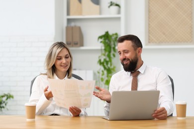 Photo of Smiling business partners working with documents at table in office