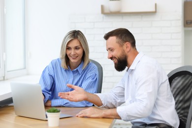 Photo of Smiling business partners working with laptop at table in office
