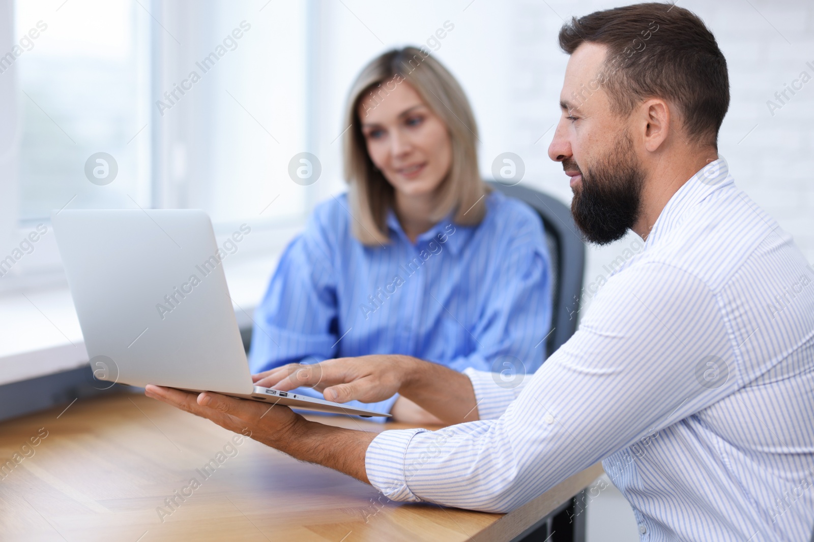 Smiling business partners working with laptop at table in office Photo of Smiling business partners working with laptop at table in office