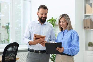 Photo of Smiling business partners working with clipboard and tablet in office