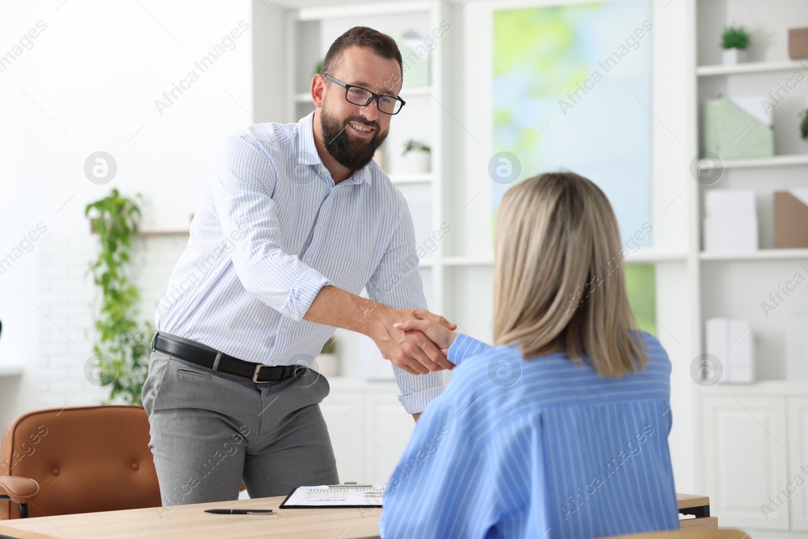 Business partners shaking hands at table in office Photo of Business partners shaking hands at table in office