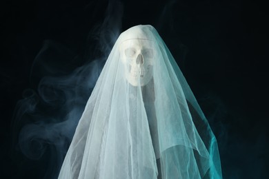 Photo of Creepy ghost. Skeleton covered with white sheet in smoke on black background