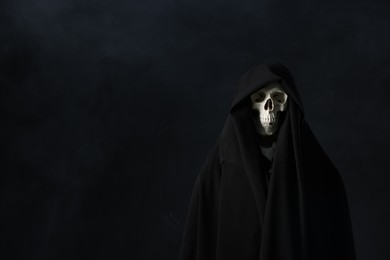 Photo of Creepy ghost. Skeleton covered with sheet in smoke on black background, space for text