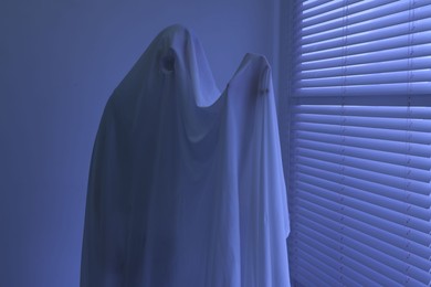 Photo of Creepy ghost. Man covered with white sheet indoors in blue light
