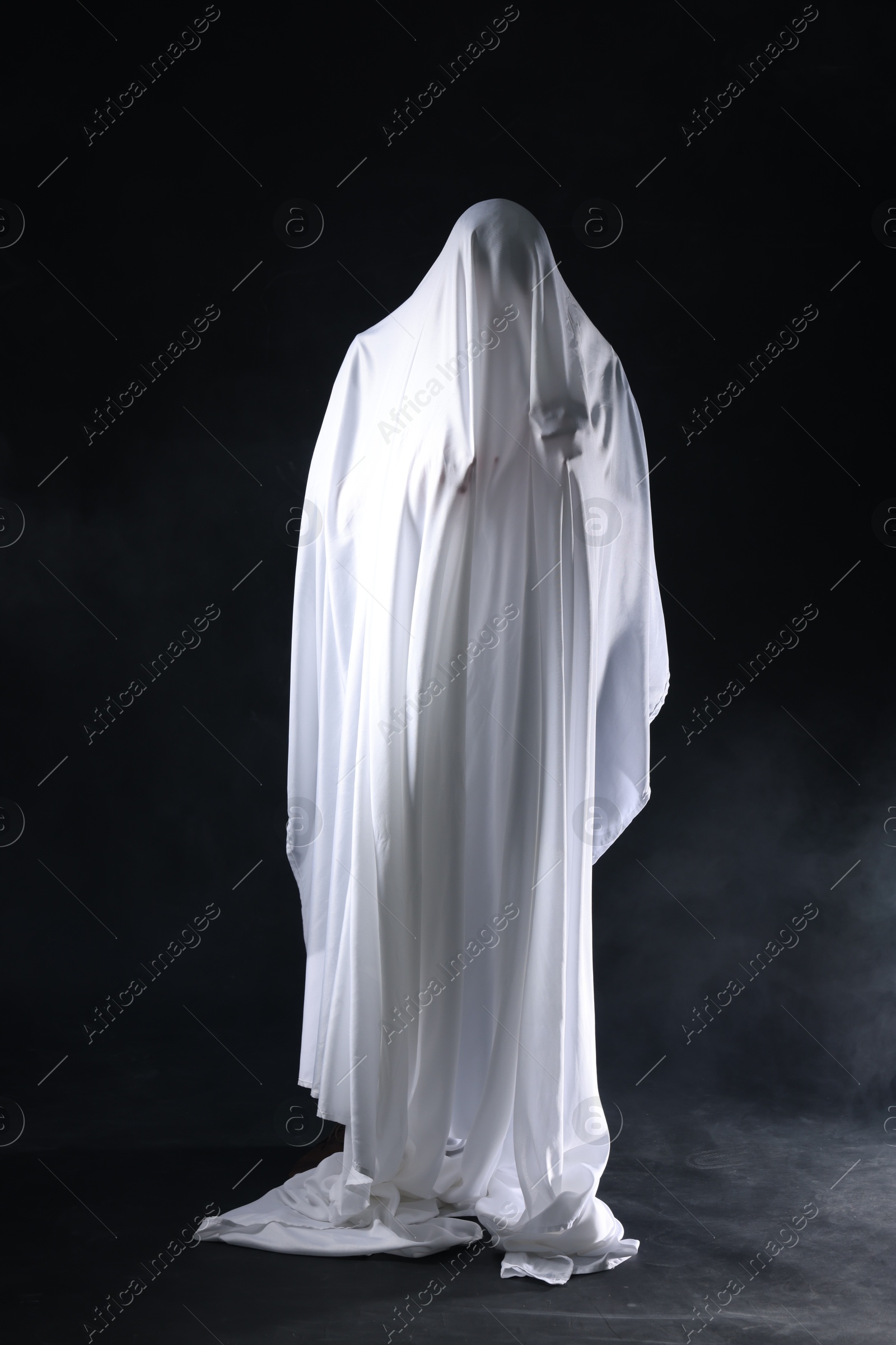 Creepy ghost. Man covered with white sheet in smoke on black background Photo of Creepy ghost. Man covered with white sheet in smoke on black background