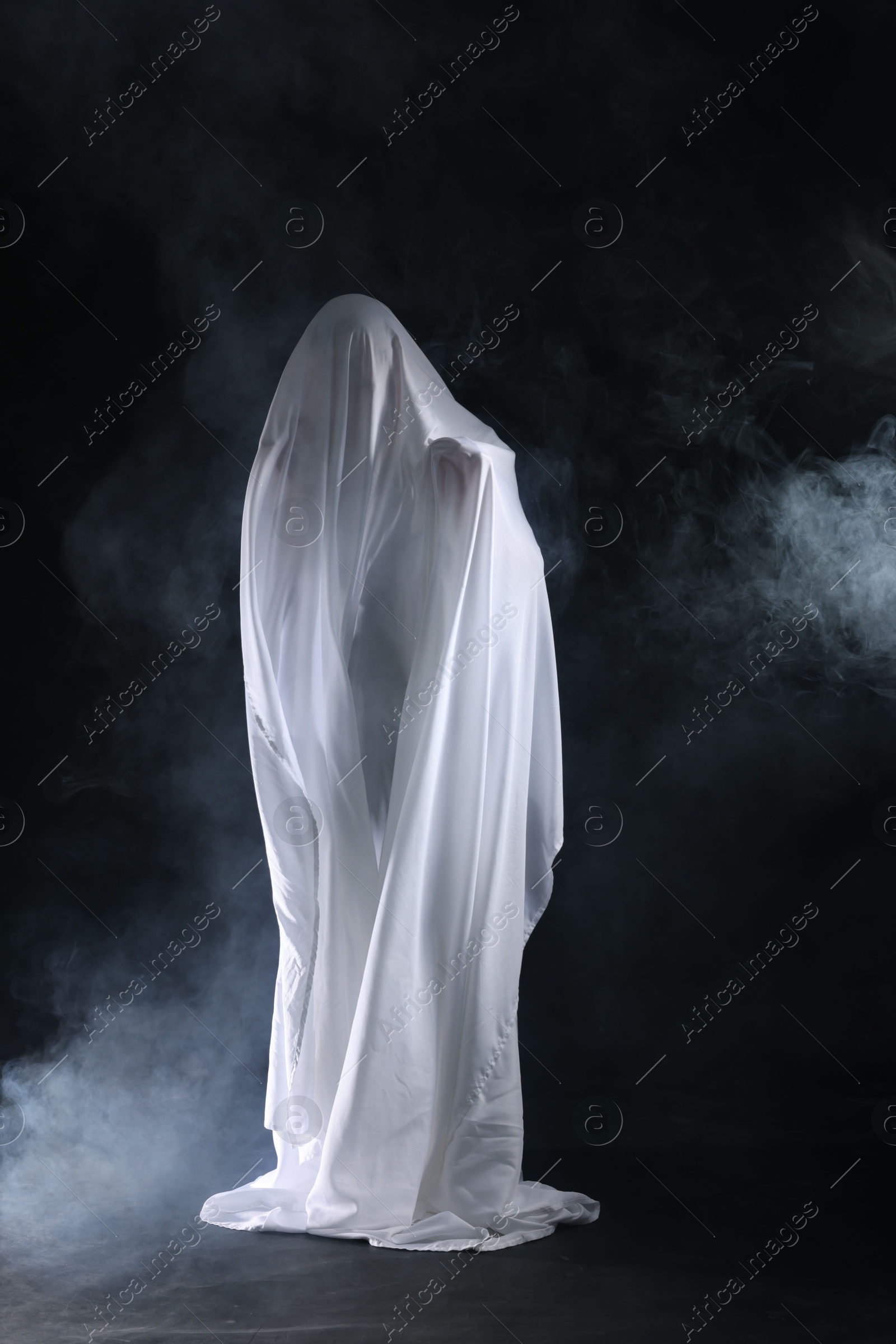 Creepy ghost. Man covered with white sheet in smoke on black background Photo of Creepy ghost. Man covered with white sheet in smoke on black background