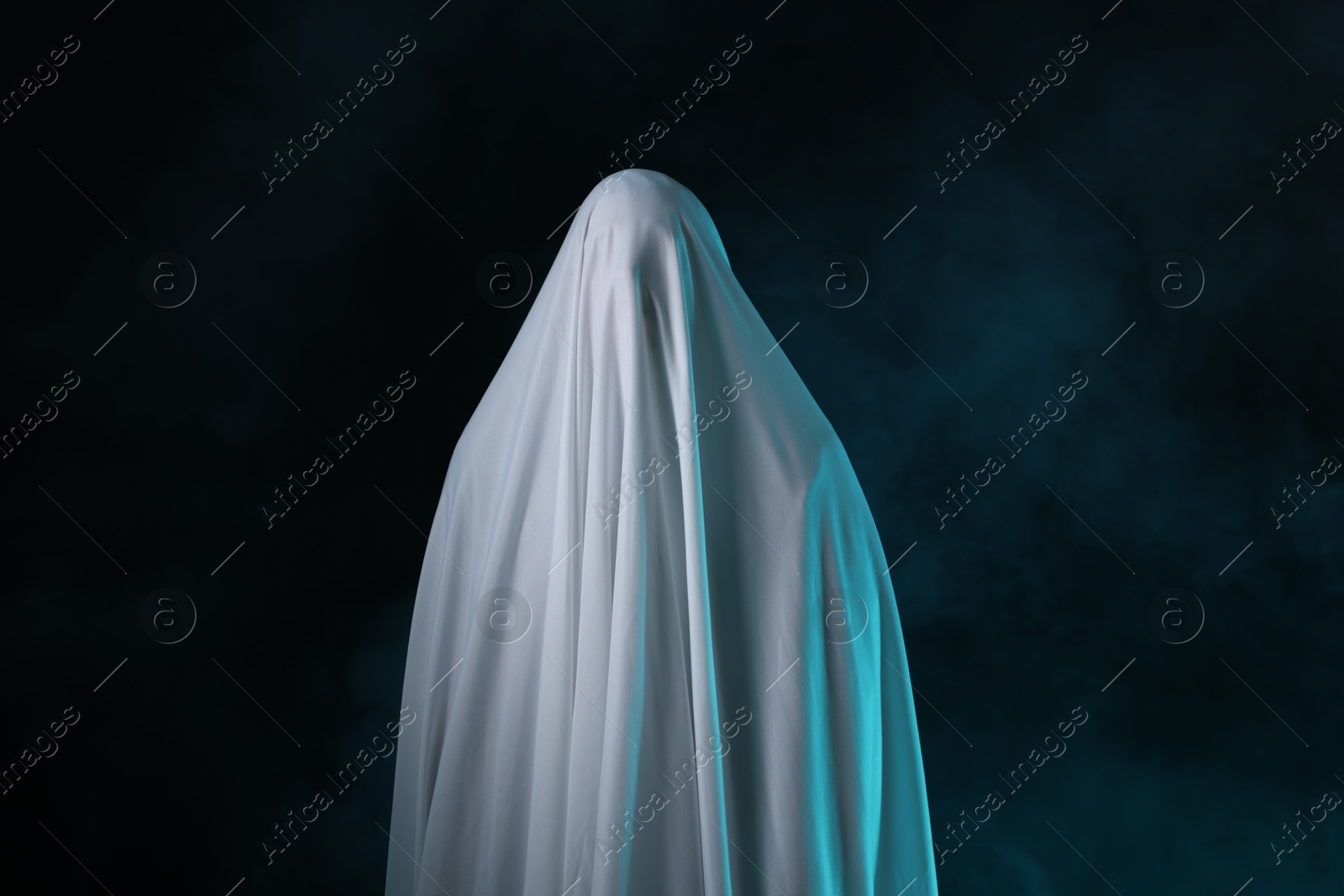 Creepy ghost. Man covered with white sheet in smoke on black background Photo of Creepy ghost. Man covered with white sheet in smoke on black background