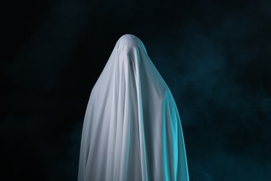 Photo of Creepy ghost. Man covered with white sheet in smoke on black background
