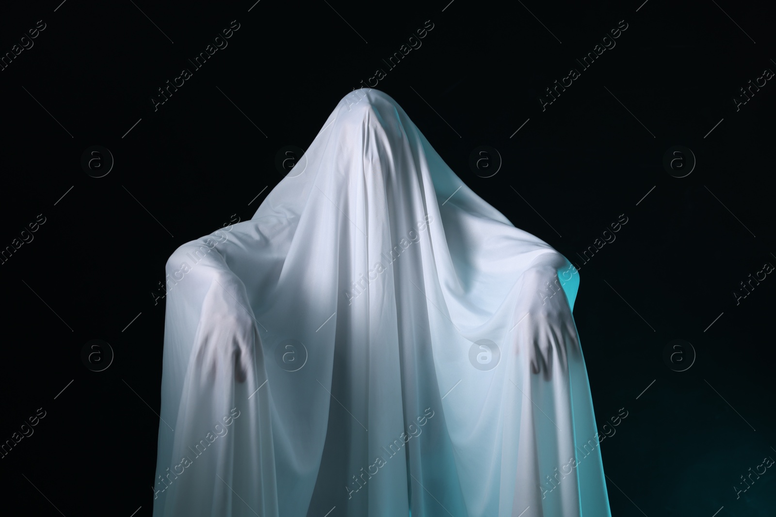 Photo of Creepy ghost. Man covered with white sheet on black background