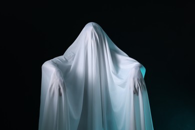 Photo of Creepy ghost. Man covered with white sheet on black background